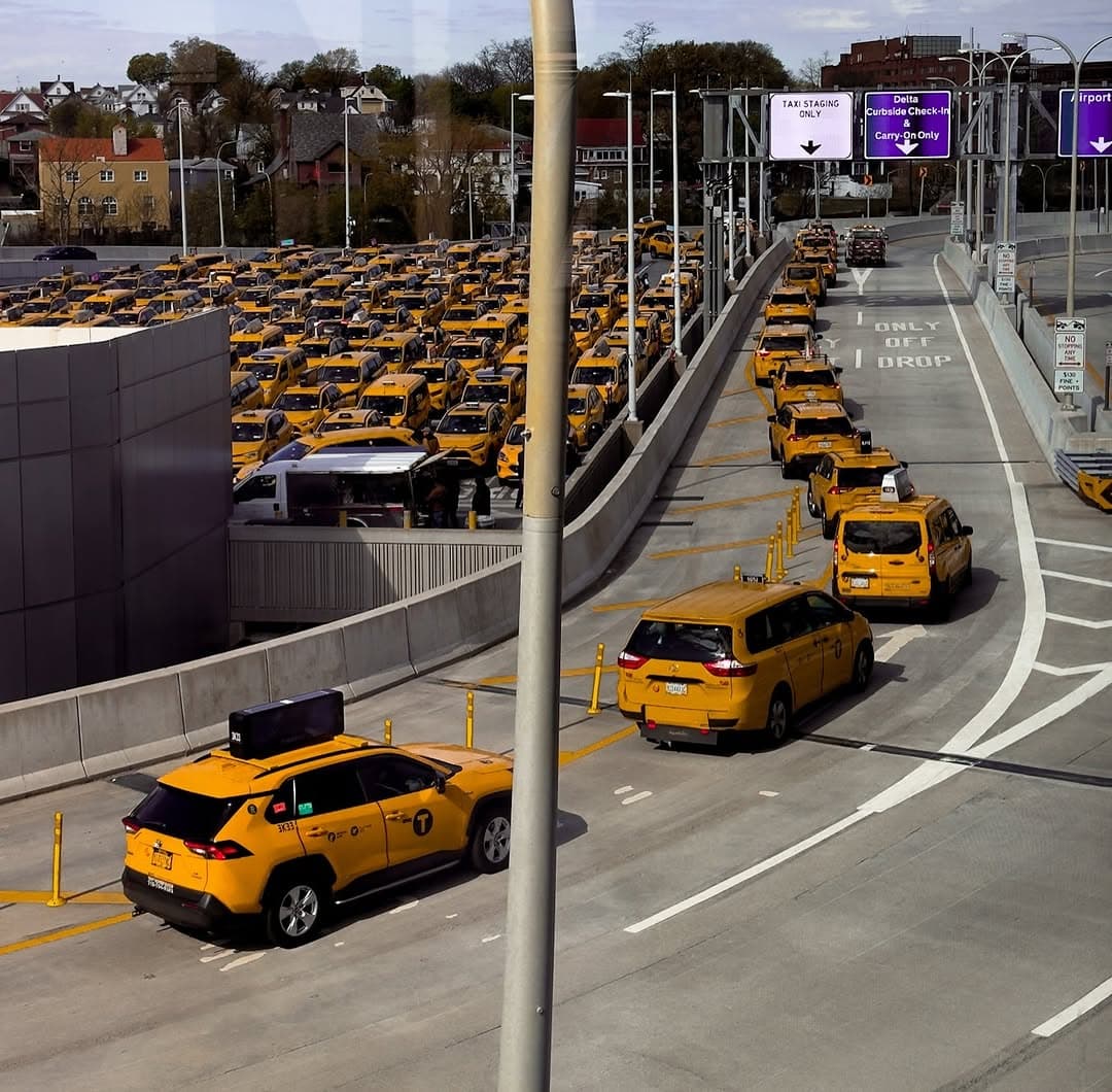 Rows of yellow taxis wait in a holding lot at LaGuardia Airport, seen from an elevated roadway.